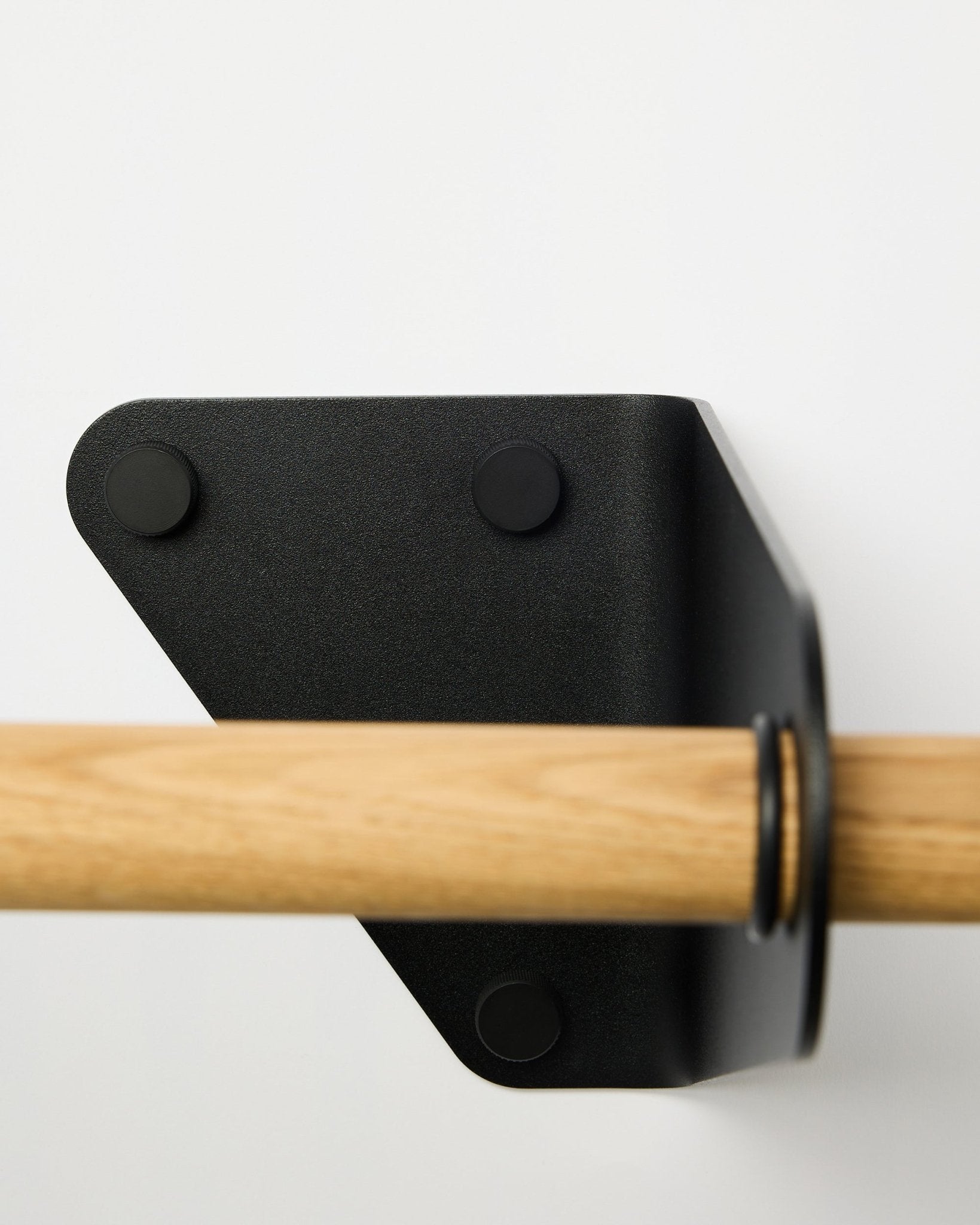 Nahaufnahme der WoodUpp Linn Coat Rail in black, 115,9 cm, an einer weißen Wand mit dreieckiger Metallhalterung montiert, gezeigt als Teil nordischer Akustik-Accessoires.