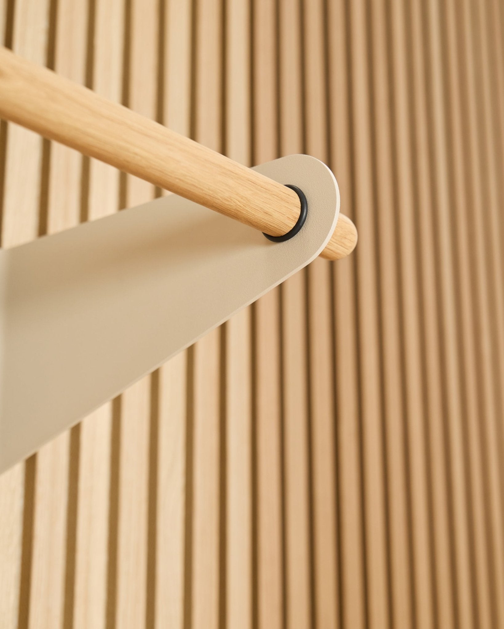 Nahaufnahme der WoodUpp Linn Garderobenstange in beige (75,9 cm), montiert an einer beigefarbenen Metallhalterung vor einem strukturierten Akupanel Akustik-Lamellenwandpaneel.