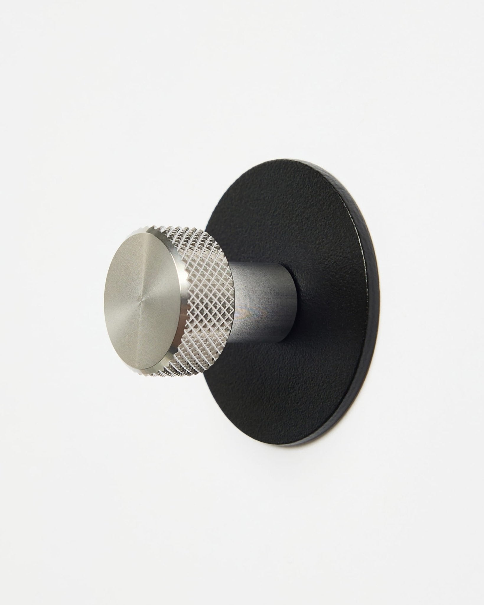 WoodUpp Norr | Coat Hook X1 in black und Edelstahl, montiert an einer schlichten weißen Wand, entworfen als Accessoire der CREATE Kollektion für Akupanel Systeme.
