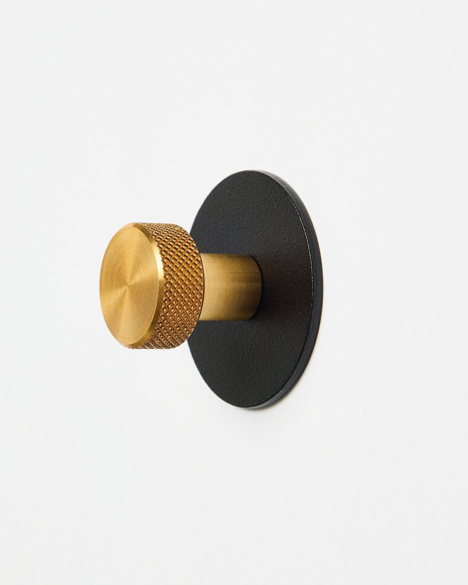 Norr Garderobenhaken X1 von WoodUpp mit strukturierter brass-Kappe und black pulverbeschichteter steel-Basis, Zubehör für Akupanel, vor weißem Hintergrund dargestellt.