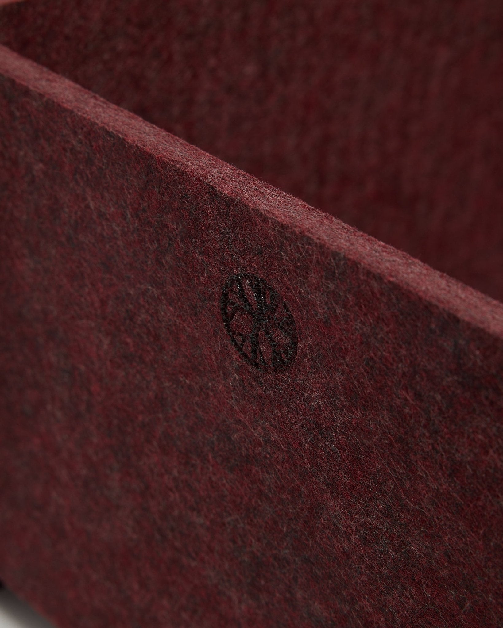 Gros plan sur la WoodUpp Vigg | Felt Box / BM2 en ox red, montrant le feutre PET texturé et un emblème circulaire black dans le coin. Design d’accessoire acoustique nordique.