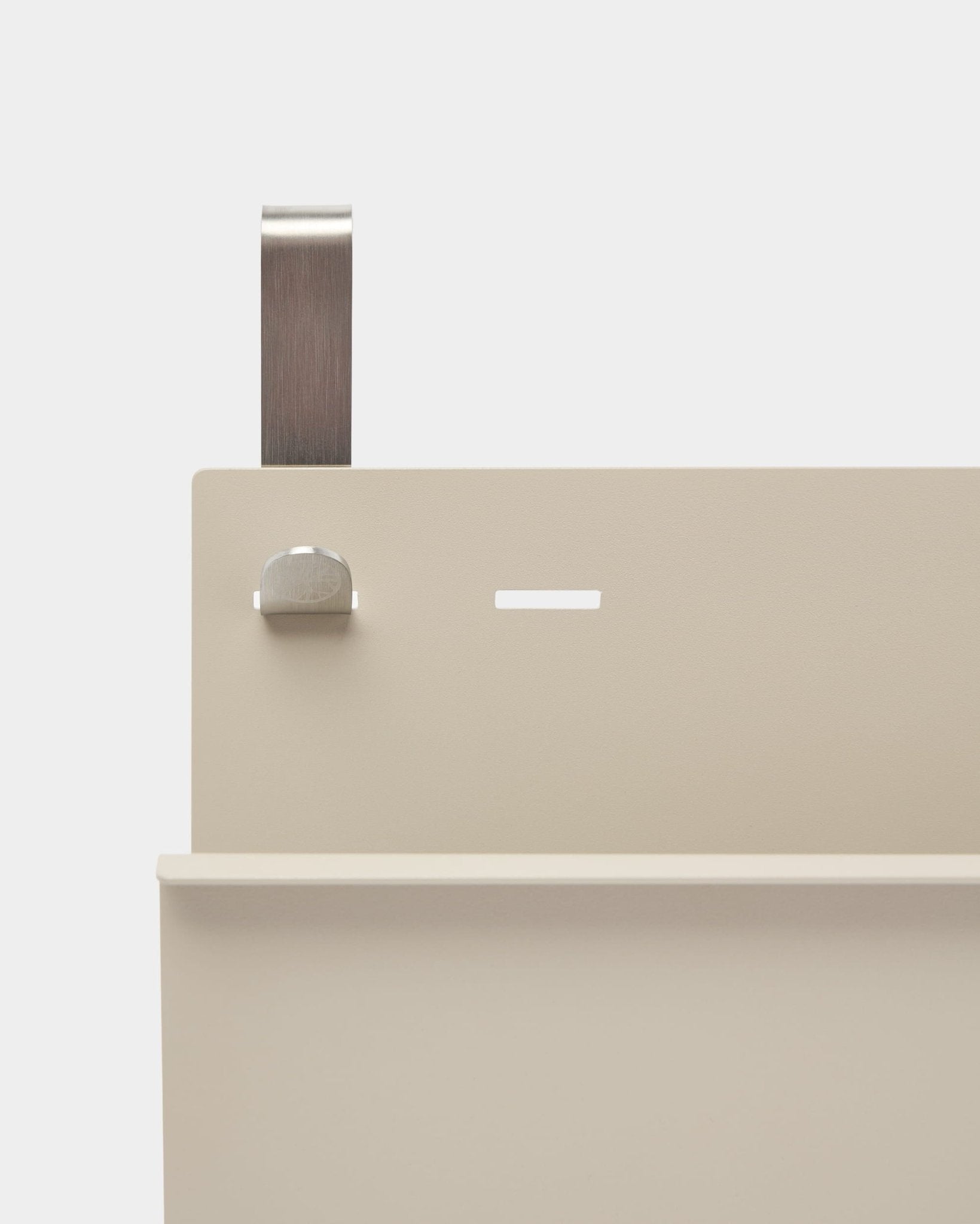 Gros plan sur le porte-revues Nell de WoodUpp en beige et en steel thermolaqué, avec étagère, fente, boulon et poignée incurvée ; il fait office de séparateur de pièce ou de porte-revues.