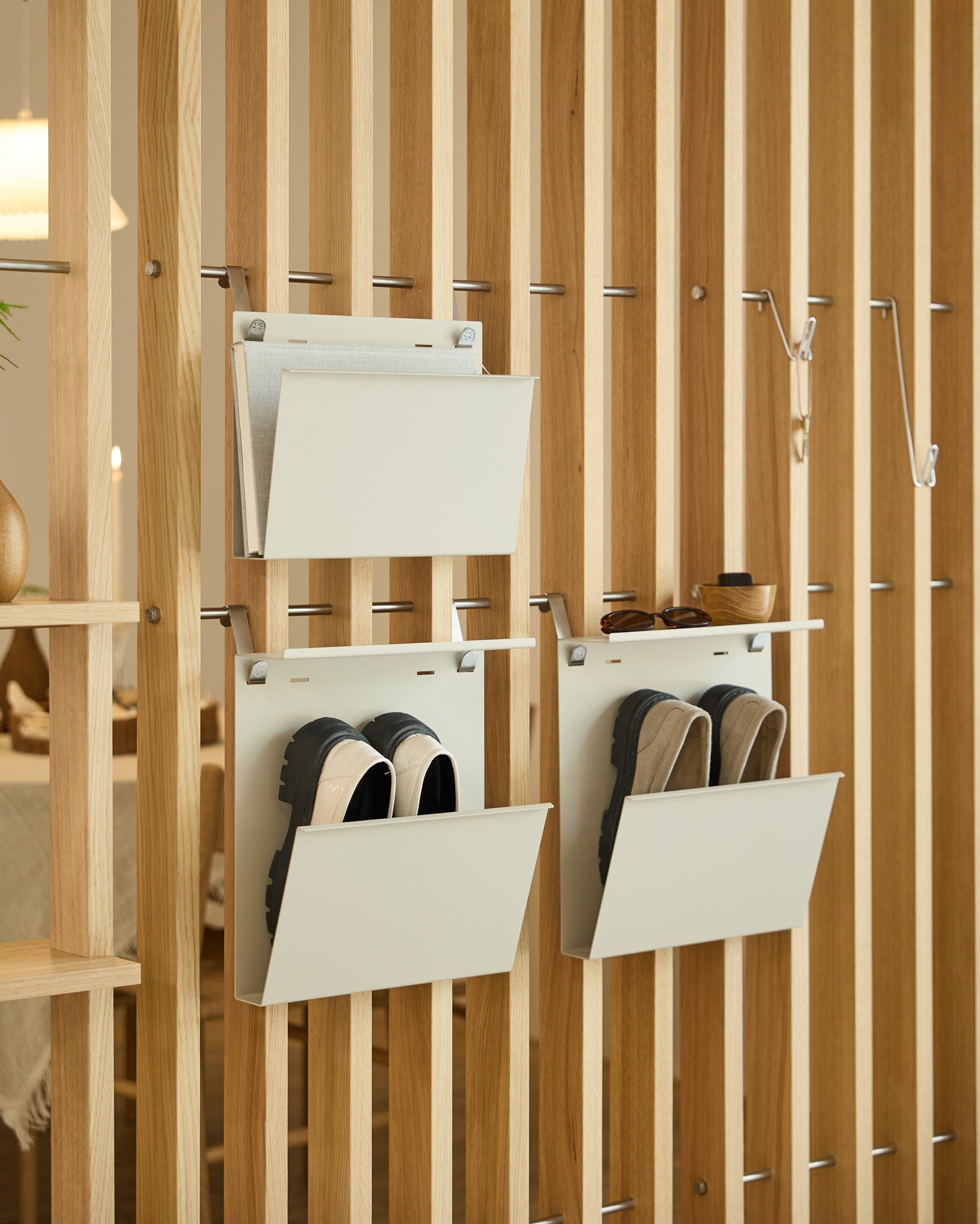 Le porte-revues Nell de WoodUpp en beige est fixé à un séparateur de pièce vertical, offrant un rangement ordonné pour les magazines et les objets small.