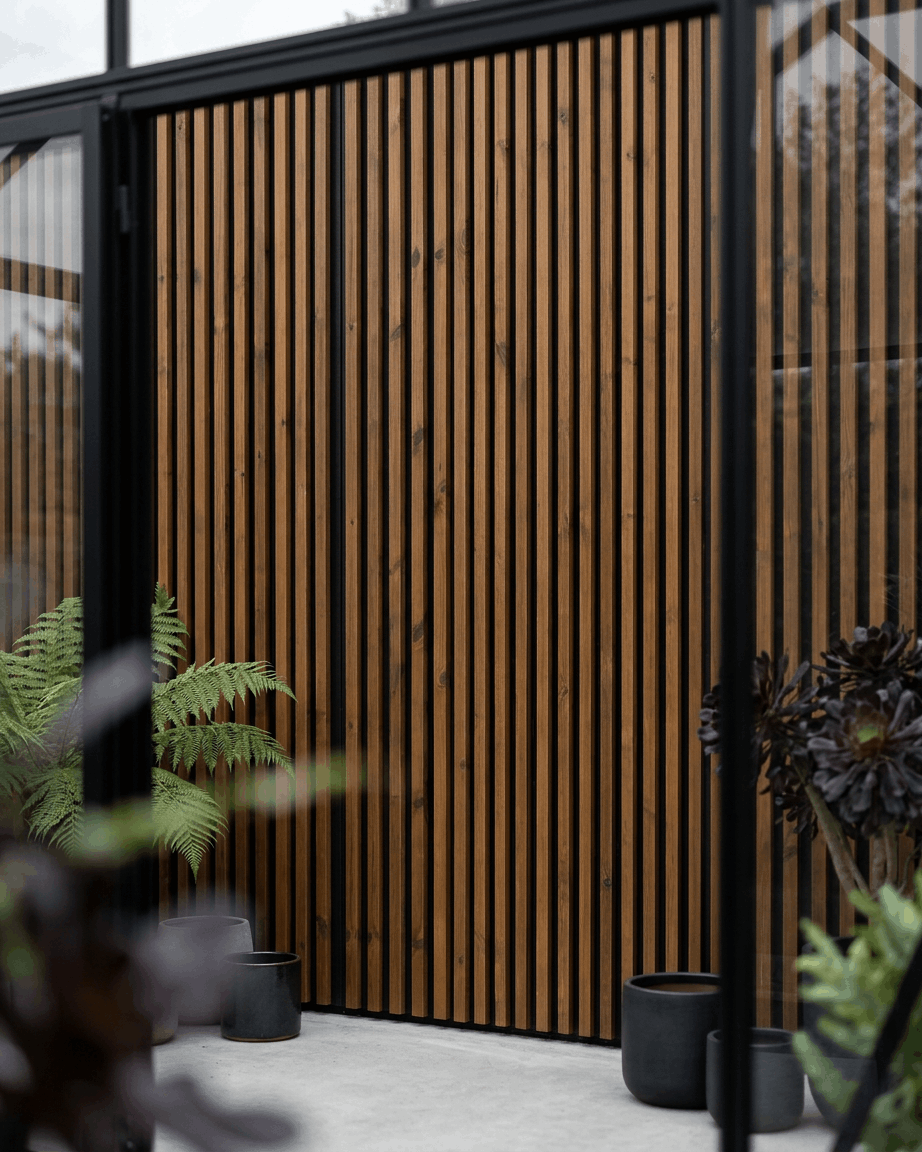 Panneau de façade extérieur WoodUpp Aluwood en brown huilé, associé à des jardinières black et à des plantes vertes, pour une terrasse nordique minimaliste.