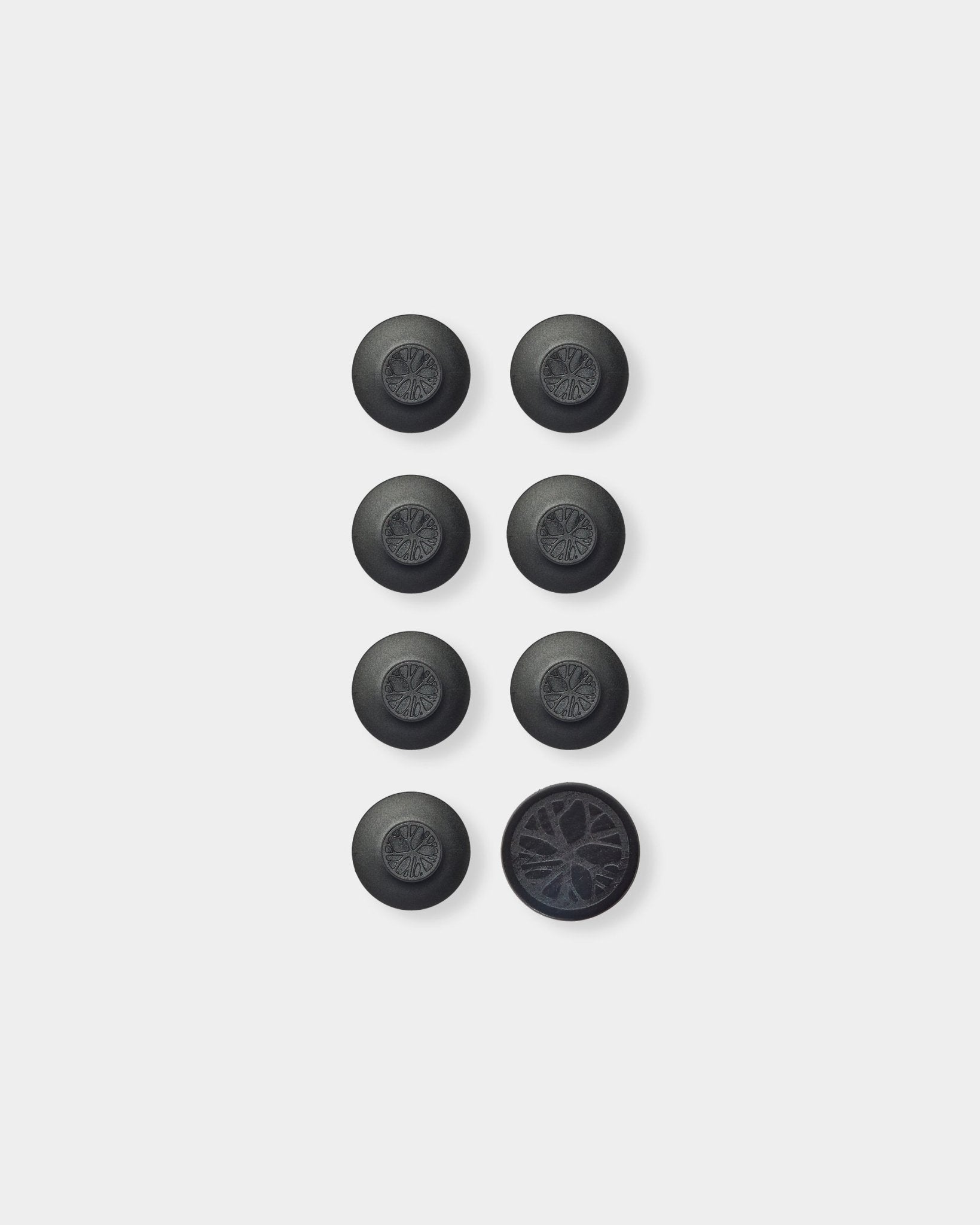 Sept accessoires ronds black Dupps pour Panneau acoustique de WoodUpp et un outil, disposés en grille ; le Dupp en bas à droite est retourné pour montrer son dessous texturé.