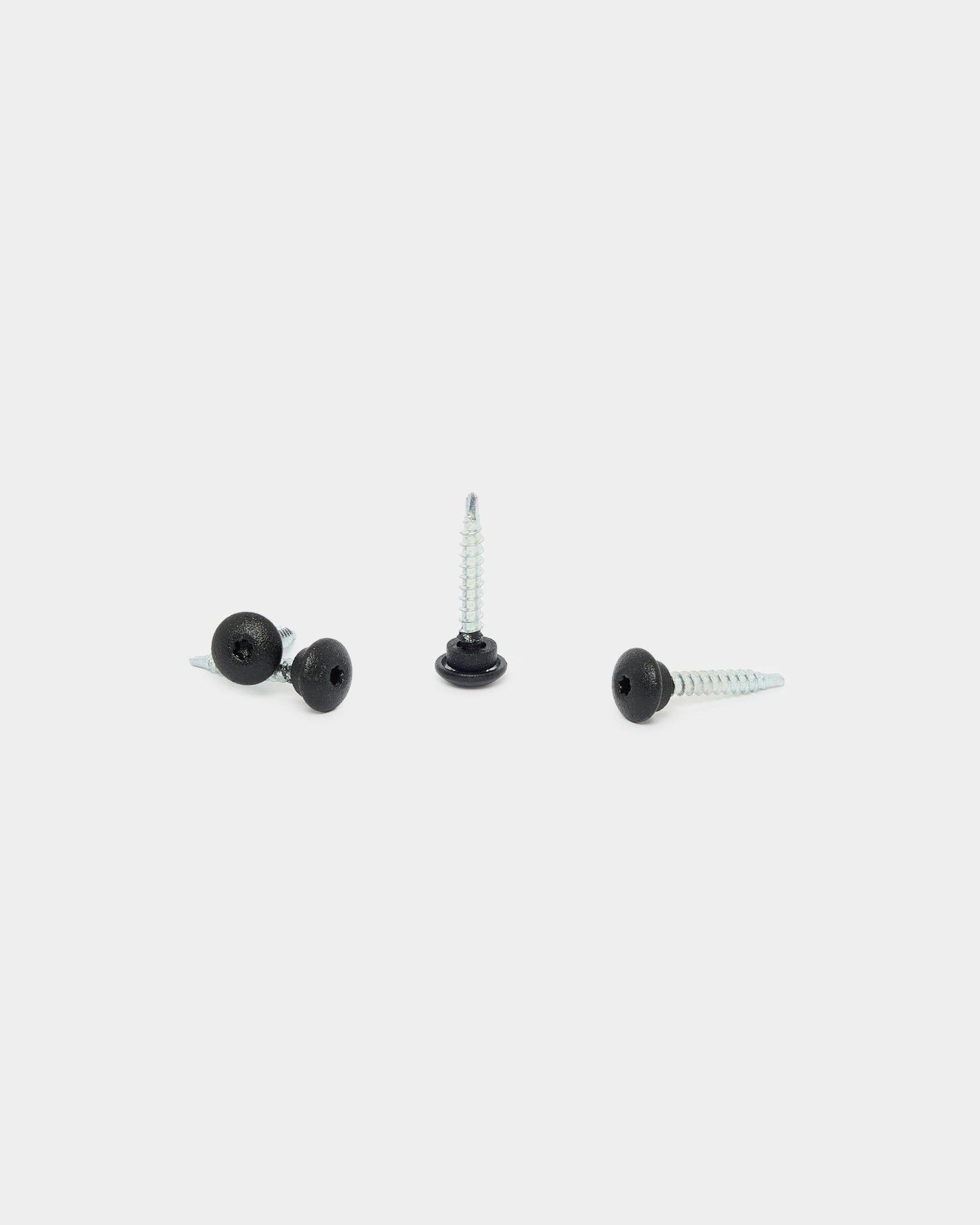 Trois vis WoodUpp 4.8x35 black avec rondelles Ø9.5 sur fond blanc, conçues comme fixations pour les panneaux de façade extérieurs Aluwood.