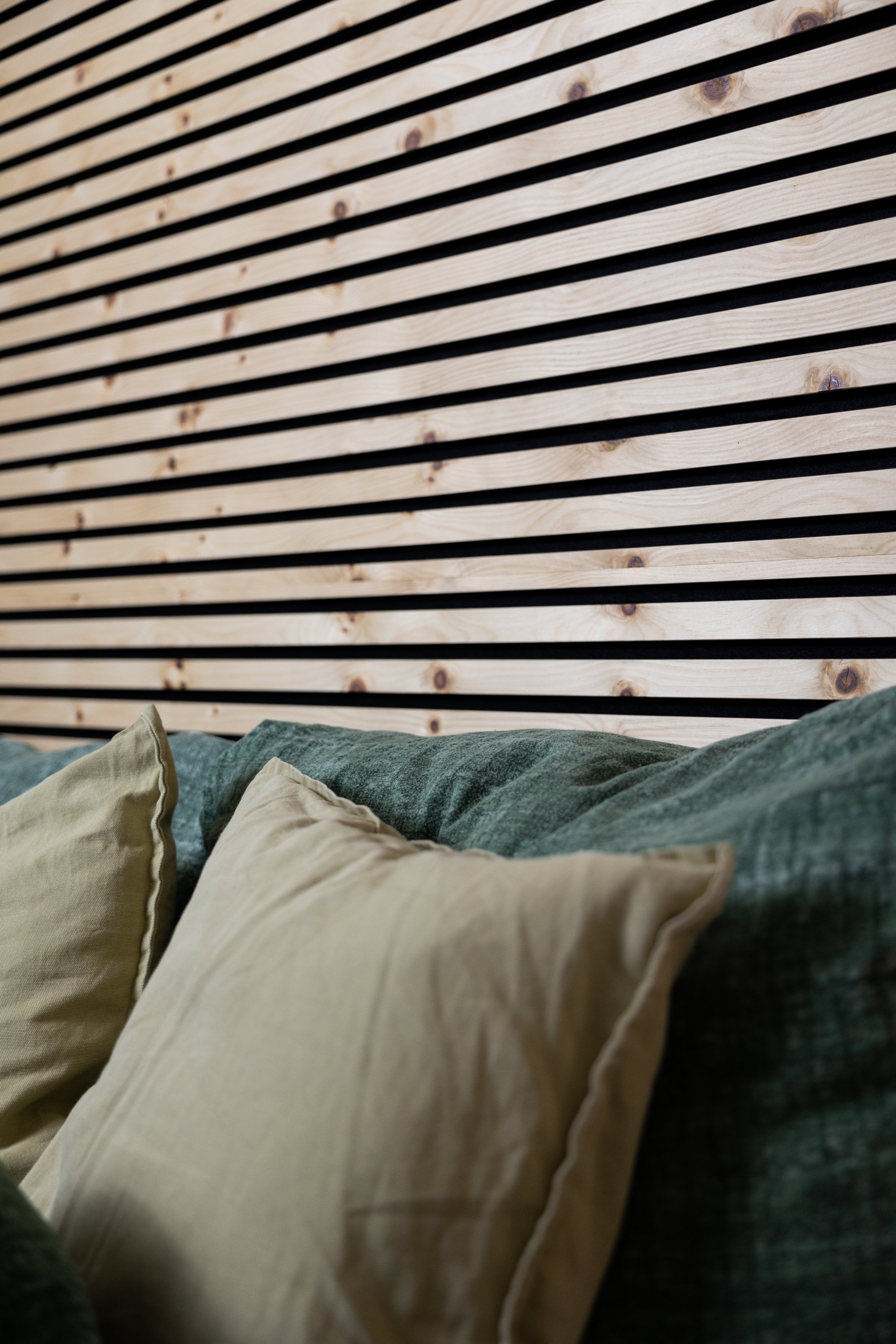 Light wood Akupanel acoustic slat wall panels with black felt backing above pillows on a bed