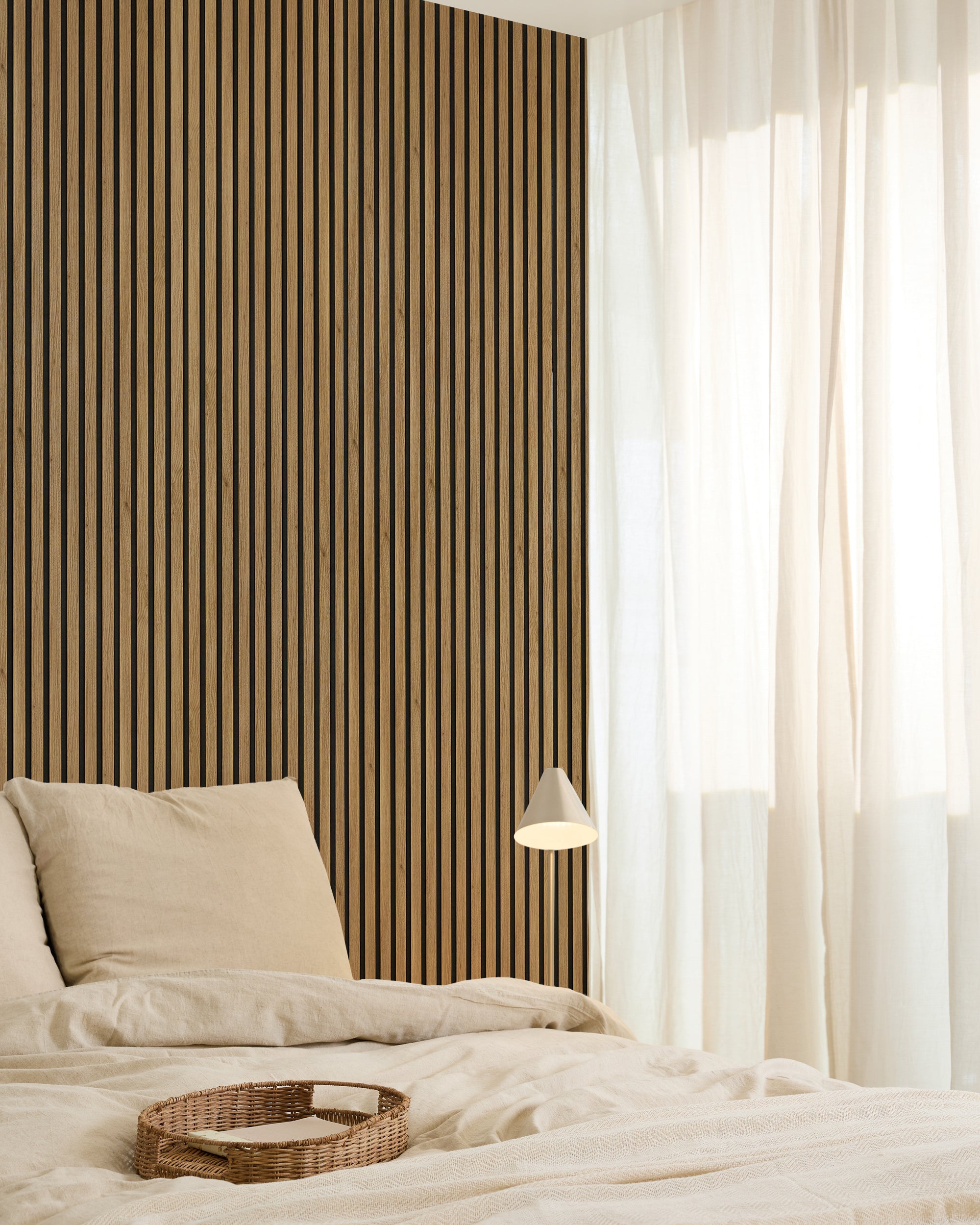 Minimalist bedroom with a beige bed, Akupanel acoustic wood slat accent wall, sheer curtains, hanging lamp, and wicker tray on the bed.