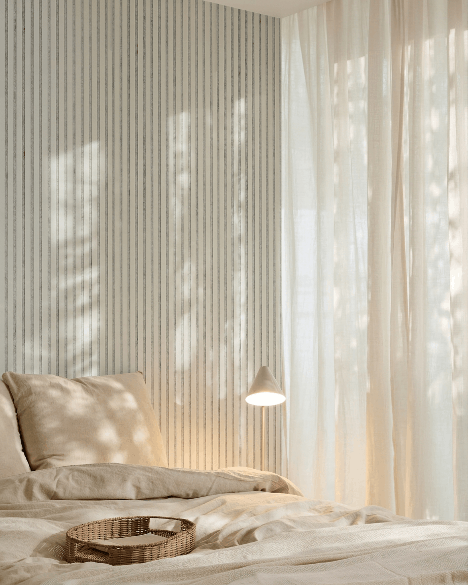 Chambre minimaliste avec du linge de lit beige, un plateau en osier, du papier peint à rayures et un panneau acoustique en bois WoodUpp Akupanel en feutre Snow Grey pour l’absorption acoustique.