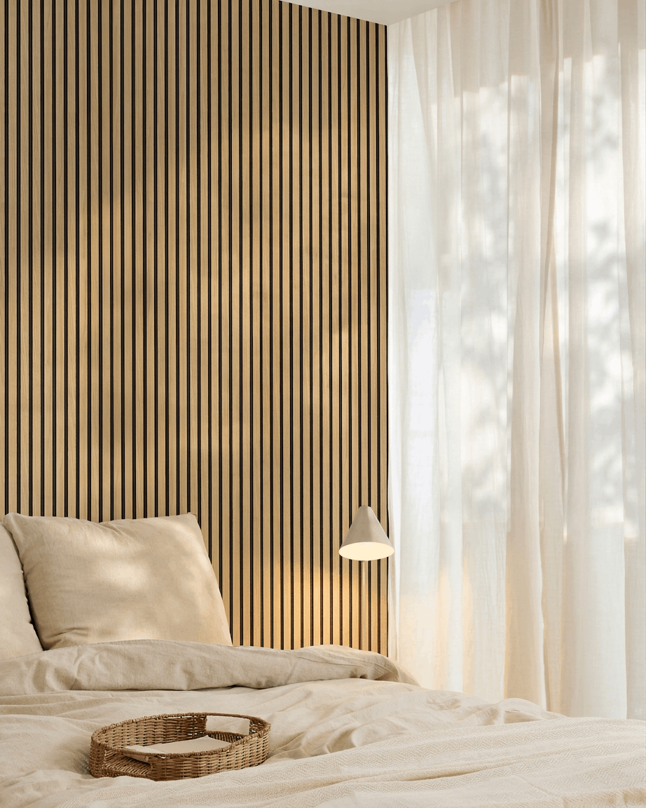 Chambre minimaliste avec du linge de lit beige, un mur accent en panneau Panneau acoustique WoodUpp Akupanel Southern Oak, un plateau tressé sur le lit et des rideaux voilés laissant entrer la lumière naturelle.