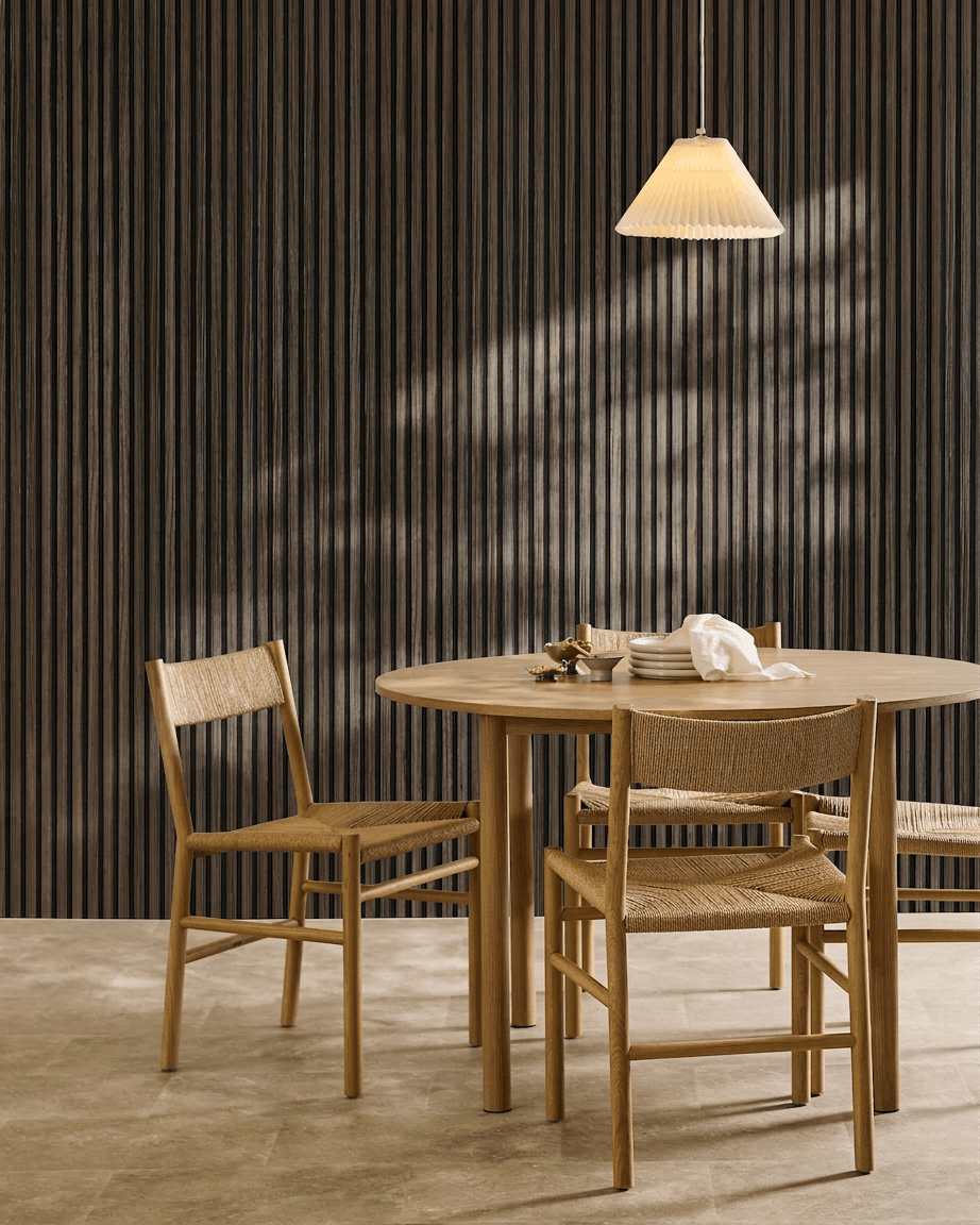Une table ronde avec quatre chaises tressées est installée à côté d’un WoodUpp Akupanel Black Oak Panneau acoustique, sous une suspension plissée.