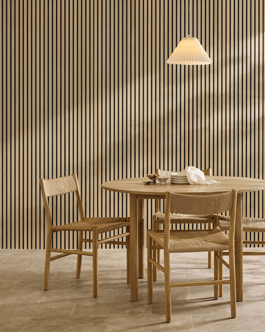 Salle à manger minimaliste avec une table ronde, des chaises tressées, une suspension et un panneau mural WoodUpp Akupanel Classic Oak Panneau acoustique.