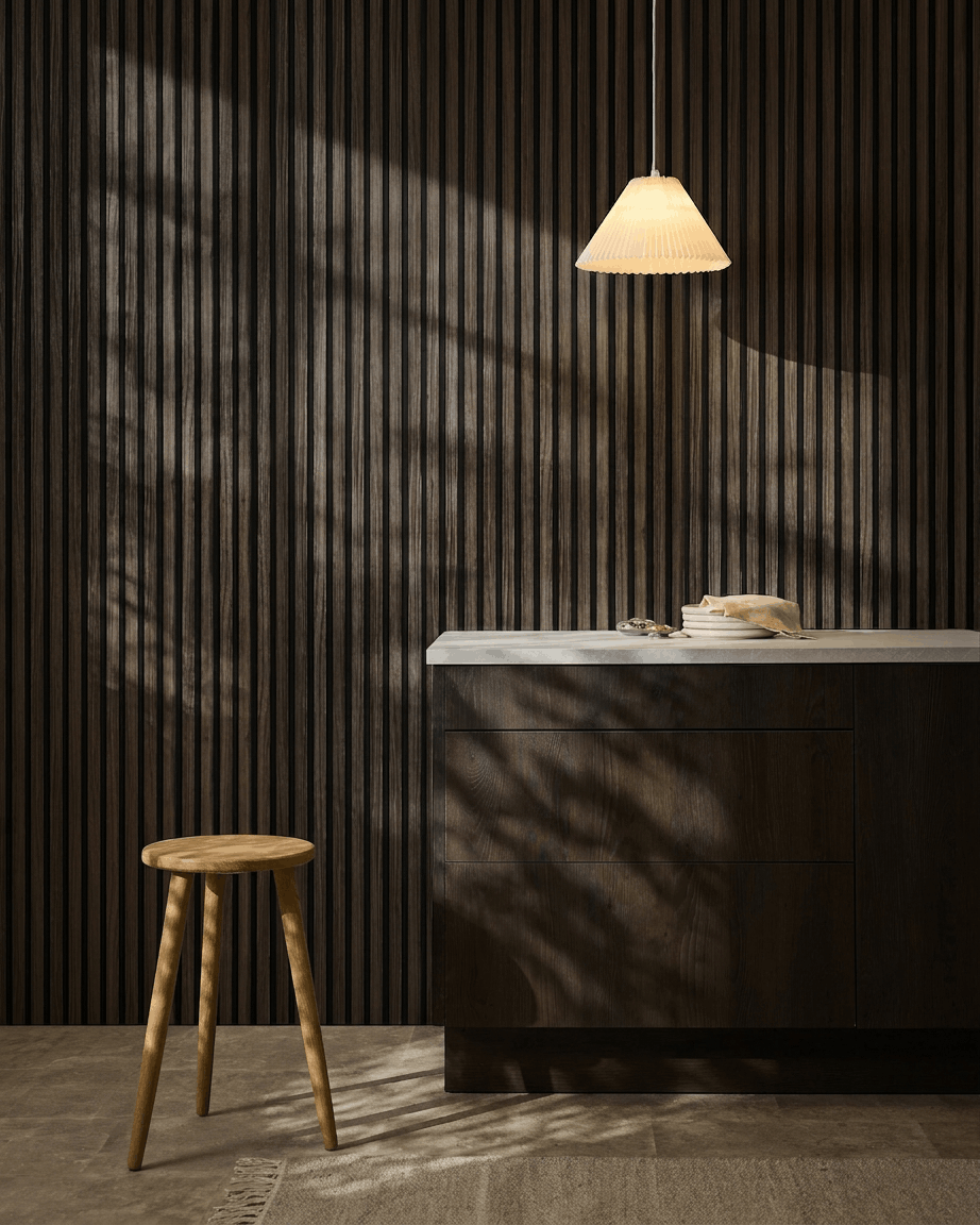 Minimalistische Küche mit WoodUpp Akupanel Black Oak Akustikpaneelen an der Wand, Holzstuhl, weißer Arbeitsplatte, beige Pendelleuchte und sonnenbeschienenen Schatten.