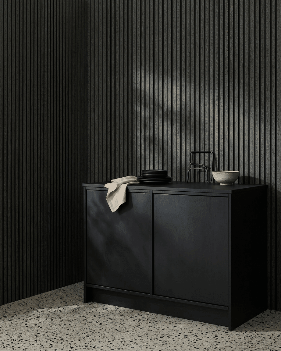 Ein black Schrank neben einem WoodUpp Akupanel Akustikholzpaneel in Charcoal/Black Felt, dekoriert mit Schalen und Tellern, auf einem hellen Terrazzoboden.
