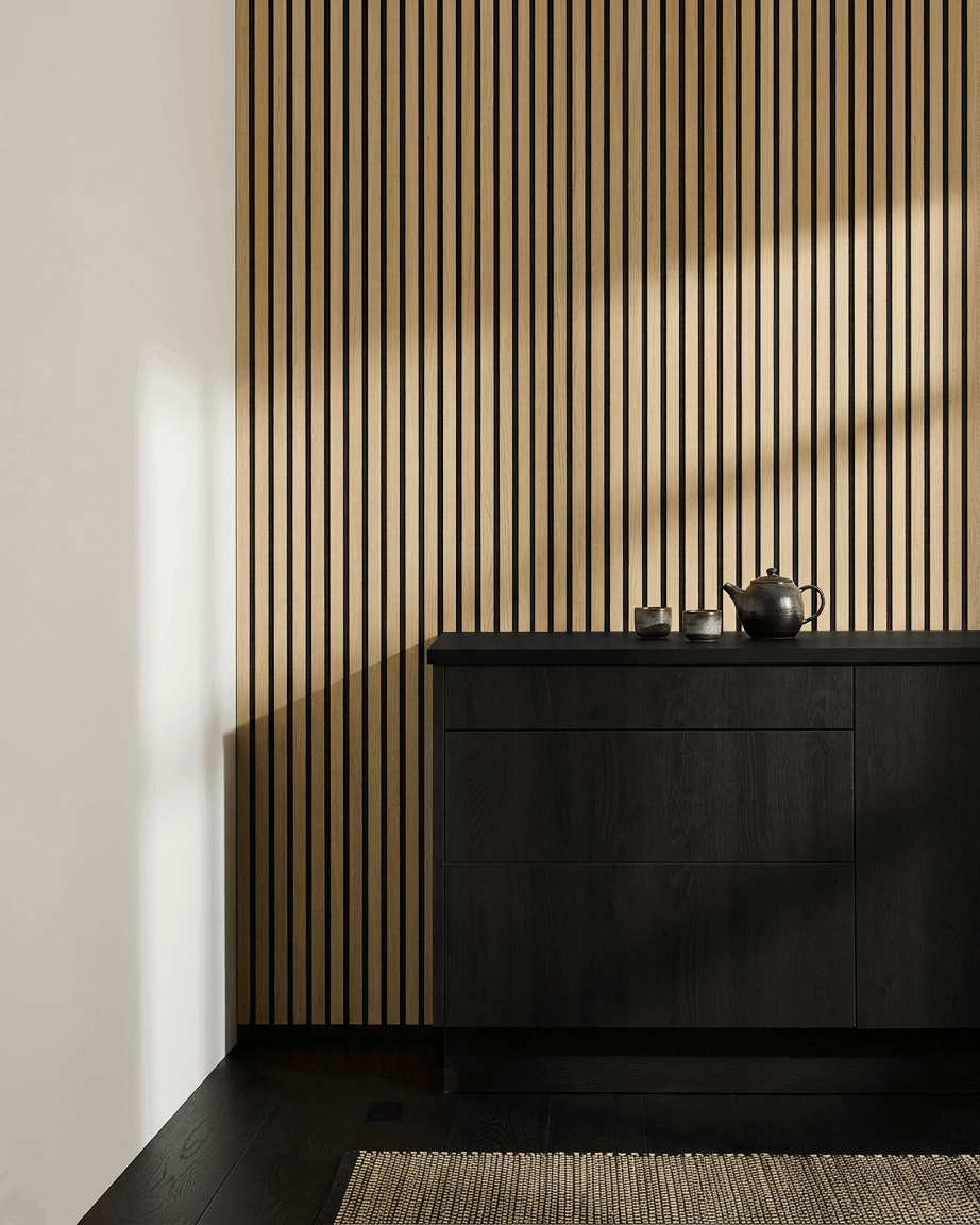 Cuisine nordique minimaliste avec WoodUpp Akupanel Panneau acoustique en chêne classique, meuble black, théière, tasses et tapis tissé sur un sol en bois foncé.