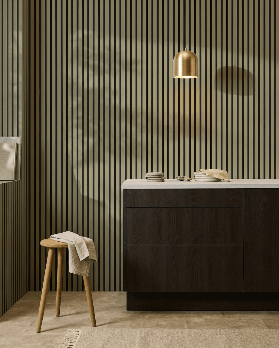 Cuisine moderne avec des meubles en bois foncé, un plan de travail en marbre, une suspension en brass, et un panneau mural acoustique à lattes WoodUpp Akupanel Colored pour l’absorption acoustique.