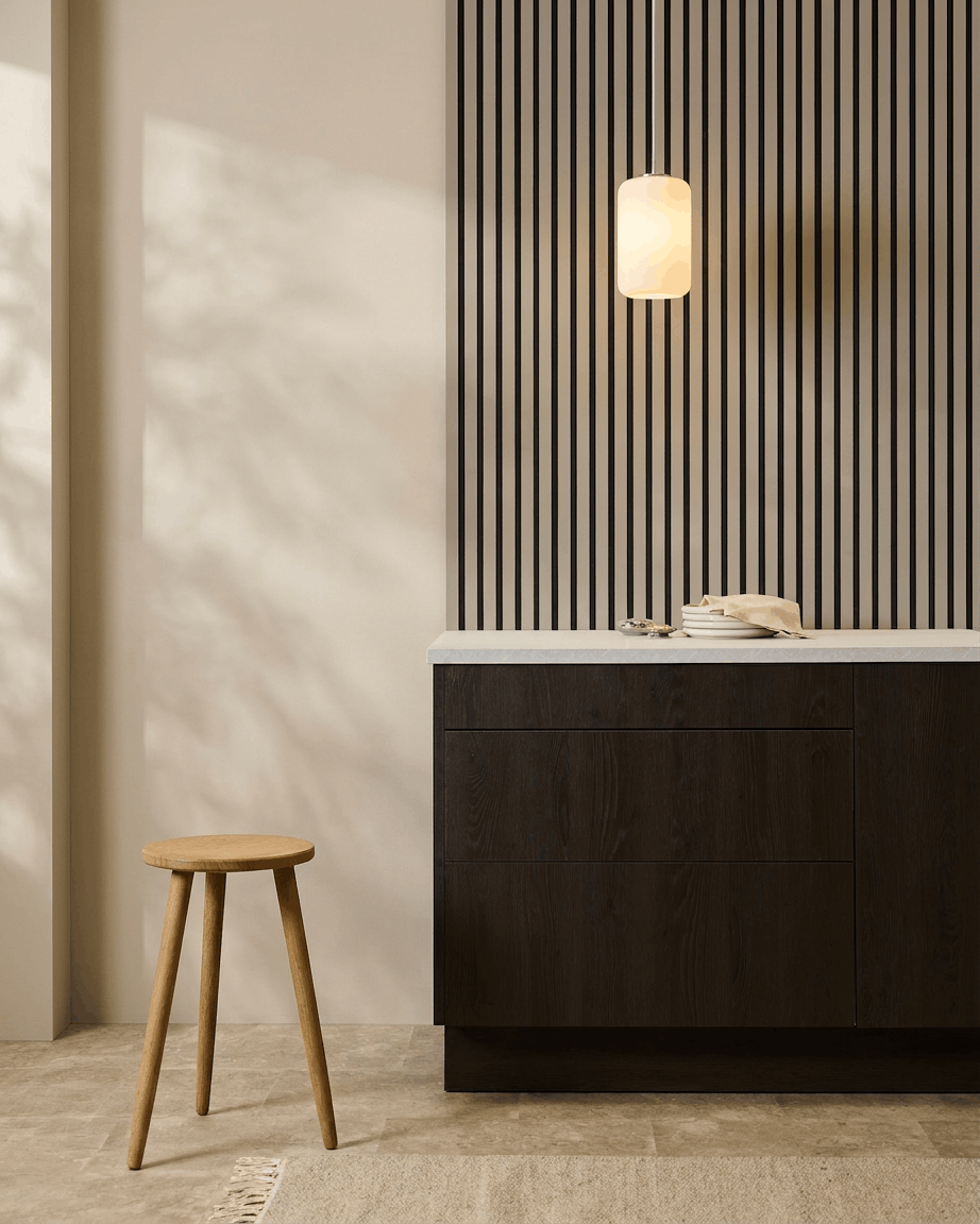 Cuisine minimaliste avec des panneaux acoustiques WoodUpp Akupanel (Stone, feutre Black) au mur, un tabouret en bois, des meubles foncés et une suspension dans des tons neutres.