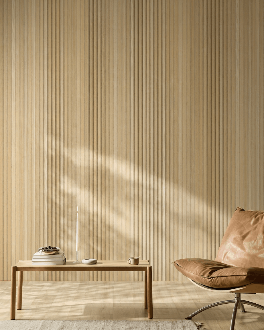 Pièce scandinave minimaliste avec un panneau acoustique en bois WoodUpp Akupanel en Natural Wood chêne classique, un fauteuil en cuir fauve et une table en bois simple avec des touches chaleureuses.