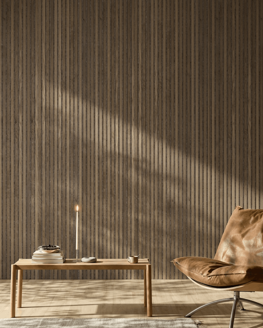 Une pièce moderne avec un fauteuil en cuir brown, une table en bois et un WoodUpp Akupanel en Rustic Grey Oak fixé au mur, baigné d’une douce lumière du soleil.
