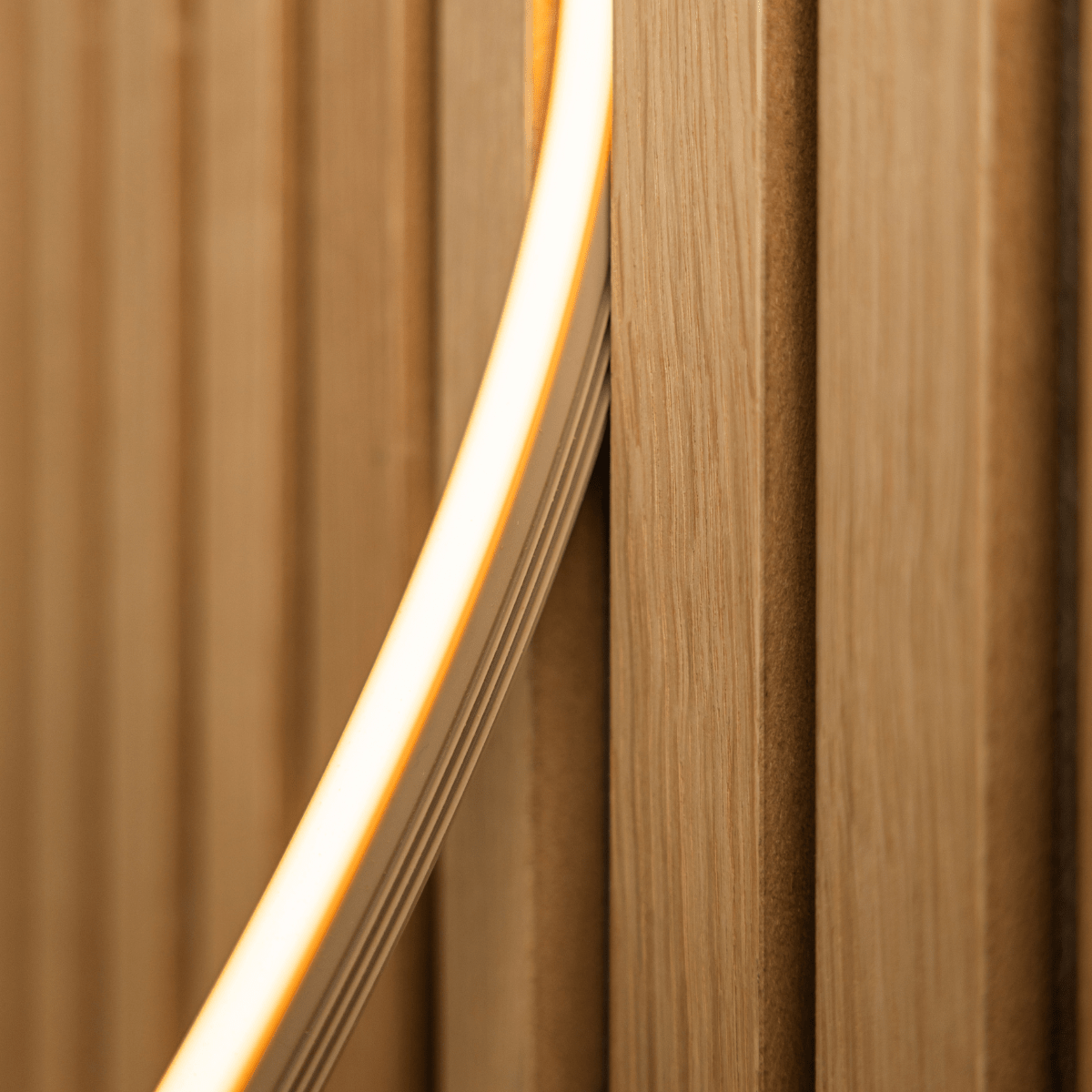 Nahaufnahme der WoodUpp Lumi LED-Lichtleiste in beige (240 cm), die warmgelbes Licht auf Akupanel vertical Akustikholzlamellen wirft; kompatibel mit Philips Hue.