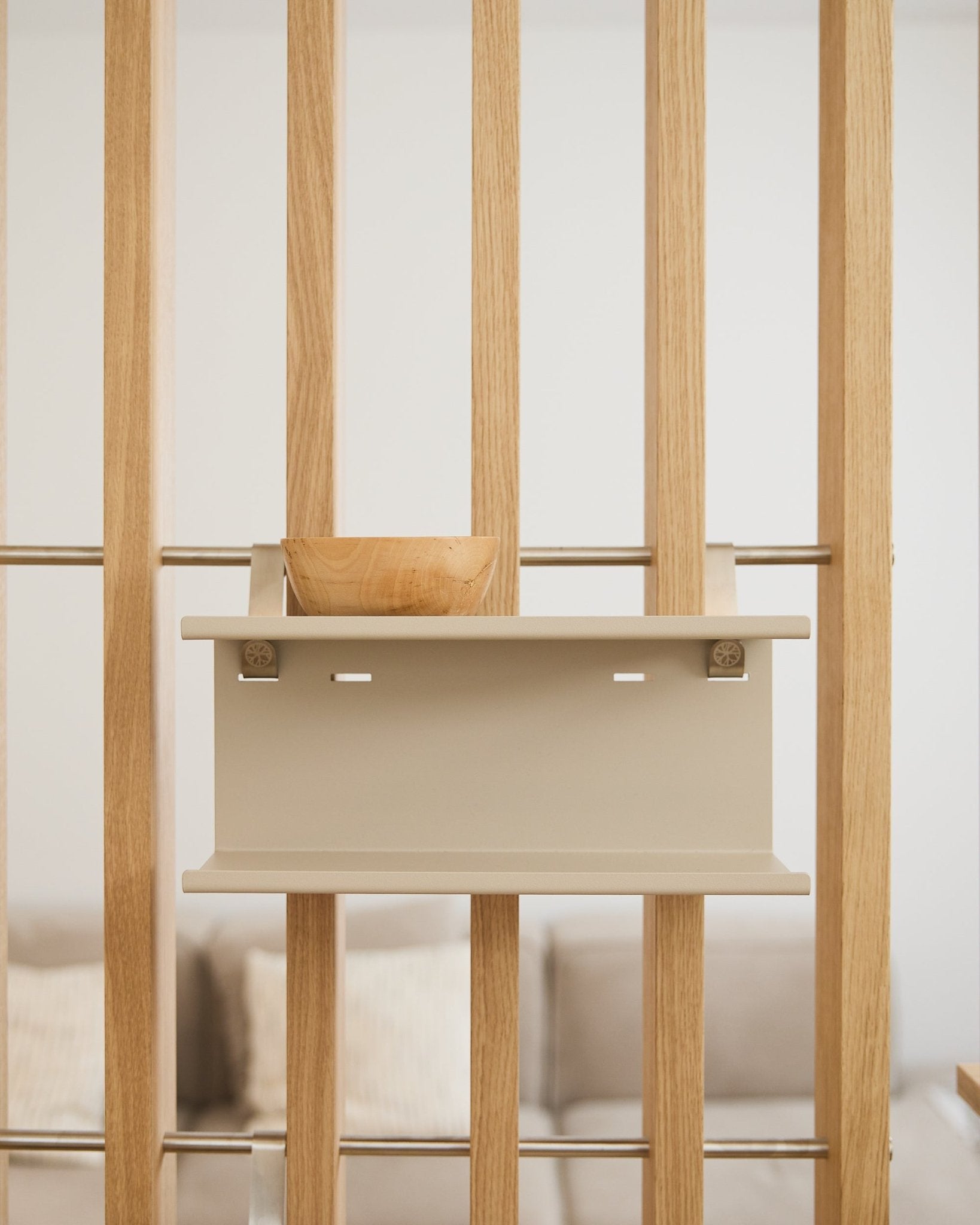 Un petit bol en bois sur l’étagère métallique double Nell en beige de WoodUpp (31,7 cm), avec un canapé et des coussins flous en arrière-plan.
