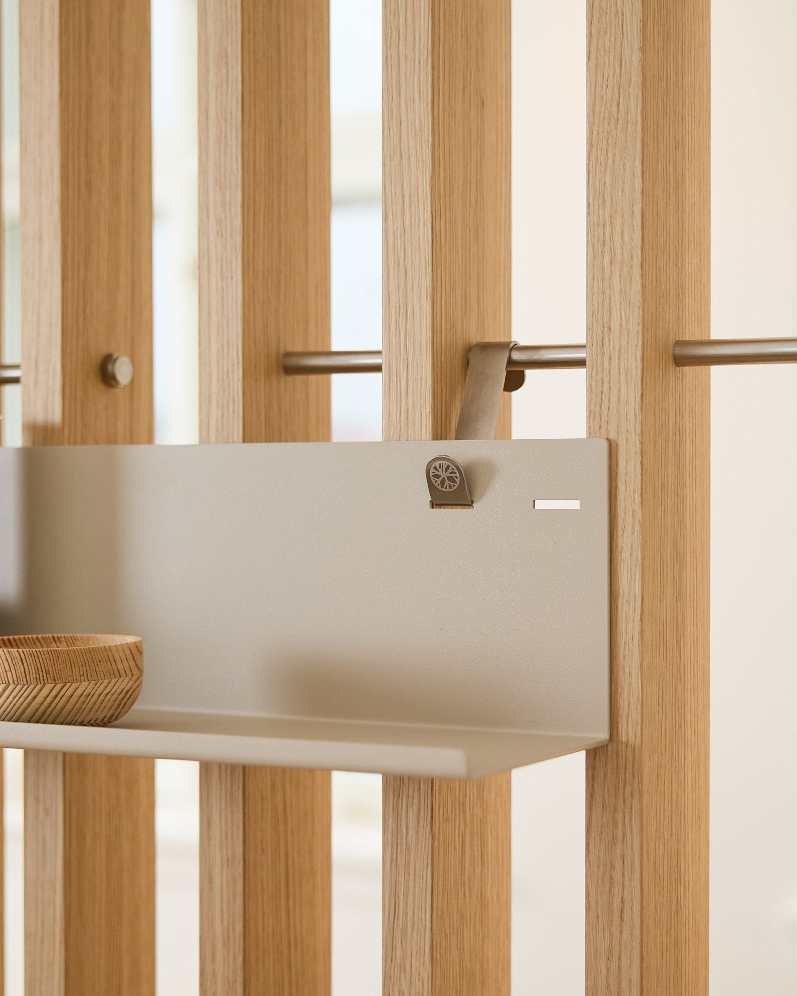 L’étagère métallique WoodUpp Beige BM1 (63 x 13,4 cm), montée sur un panneau acoustique à lattes vertical, présente un bol en bois sur le côté gauche de l’étagère.