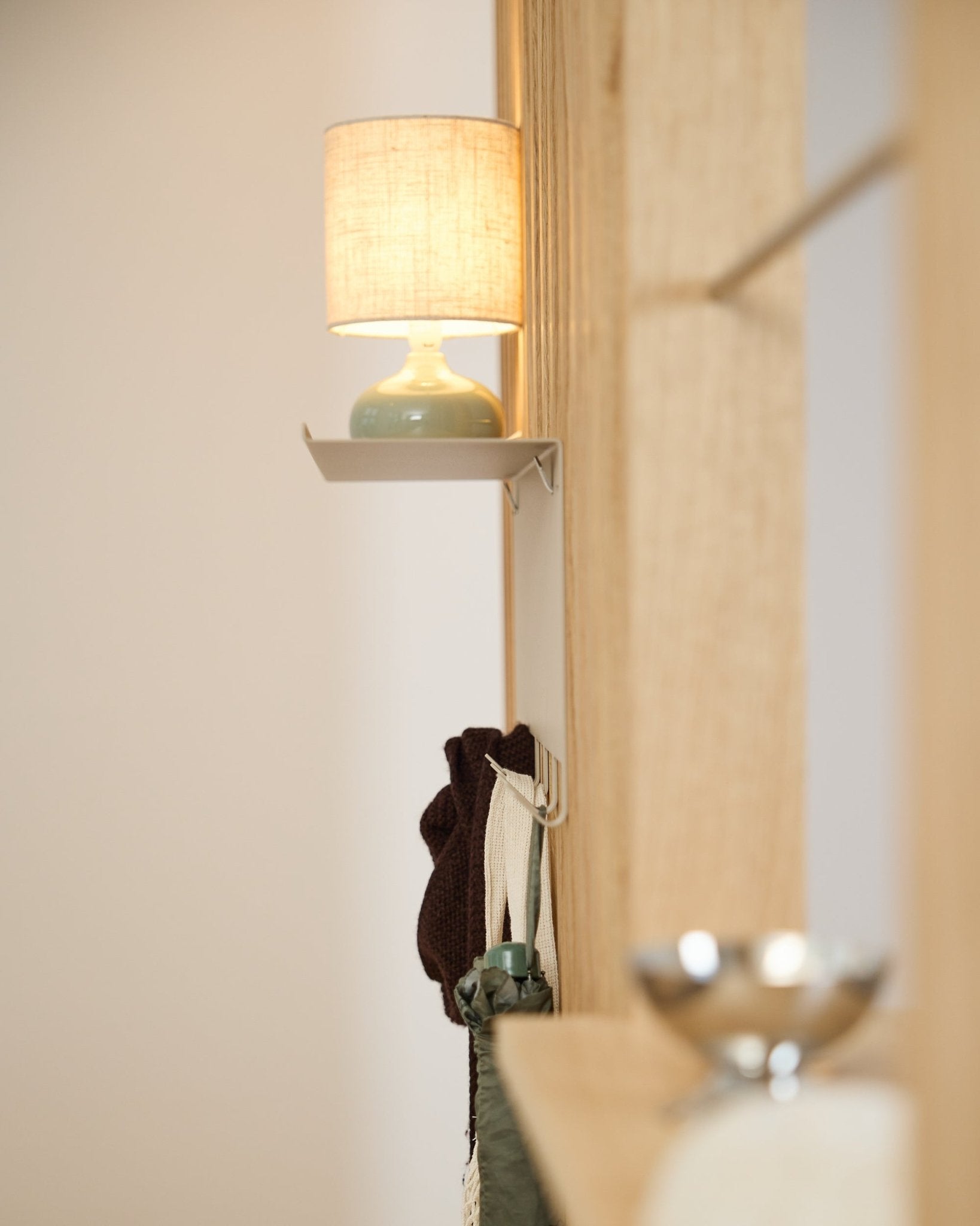 Une patère WoodUpp Nell BM1 beige (63,5 x 24 cm) se trouve sous une small lampe de table, à côté d’un mur de Panneau acoustique en bois nordique clair.