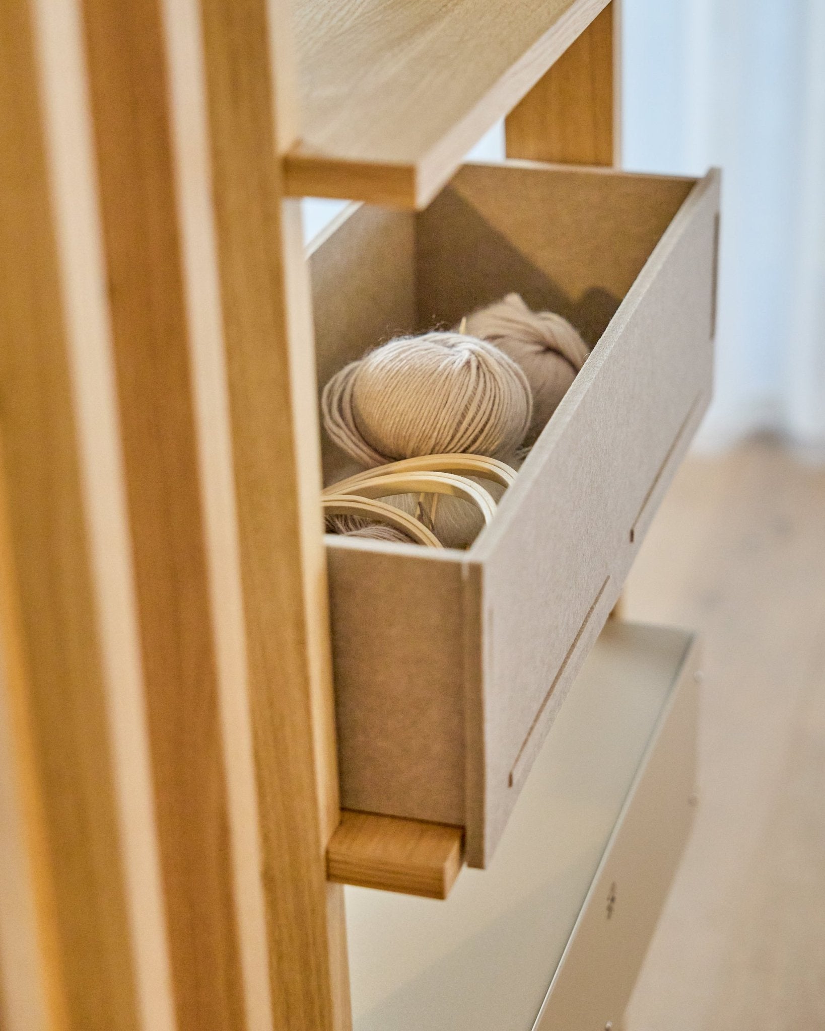 Le WoodUpp Vigg Felt Box / BM2 en beige contient des pelotes de laine légères et des tambours à broder en bois sur une étagère en bois, en harmonie avec des panneaux acoustiques nordiques.