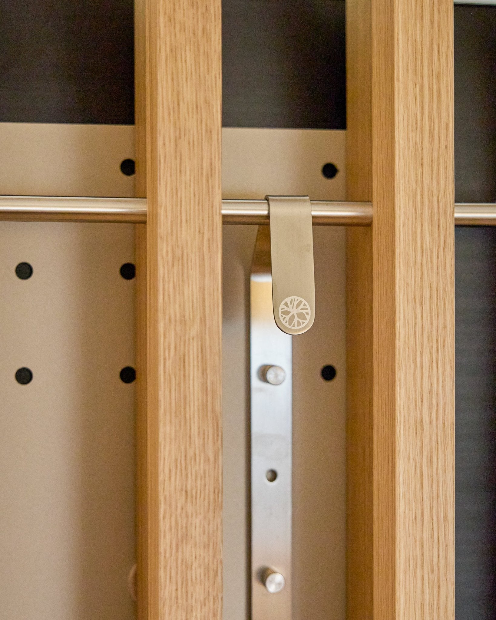 Une pince métallique en forme de soleil est fixée à une latte en bois sur le WoodUpp Nell | TV-Mount BM1, meuble en panneau Panneau acoustique 64x44 cm Beige avec réglage en hauteur.