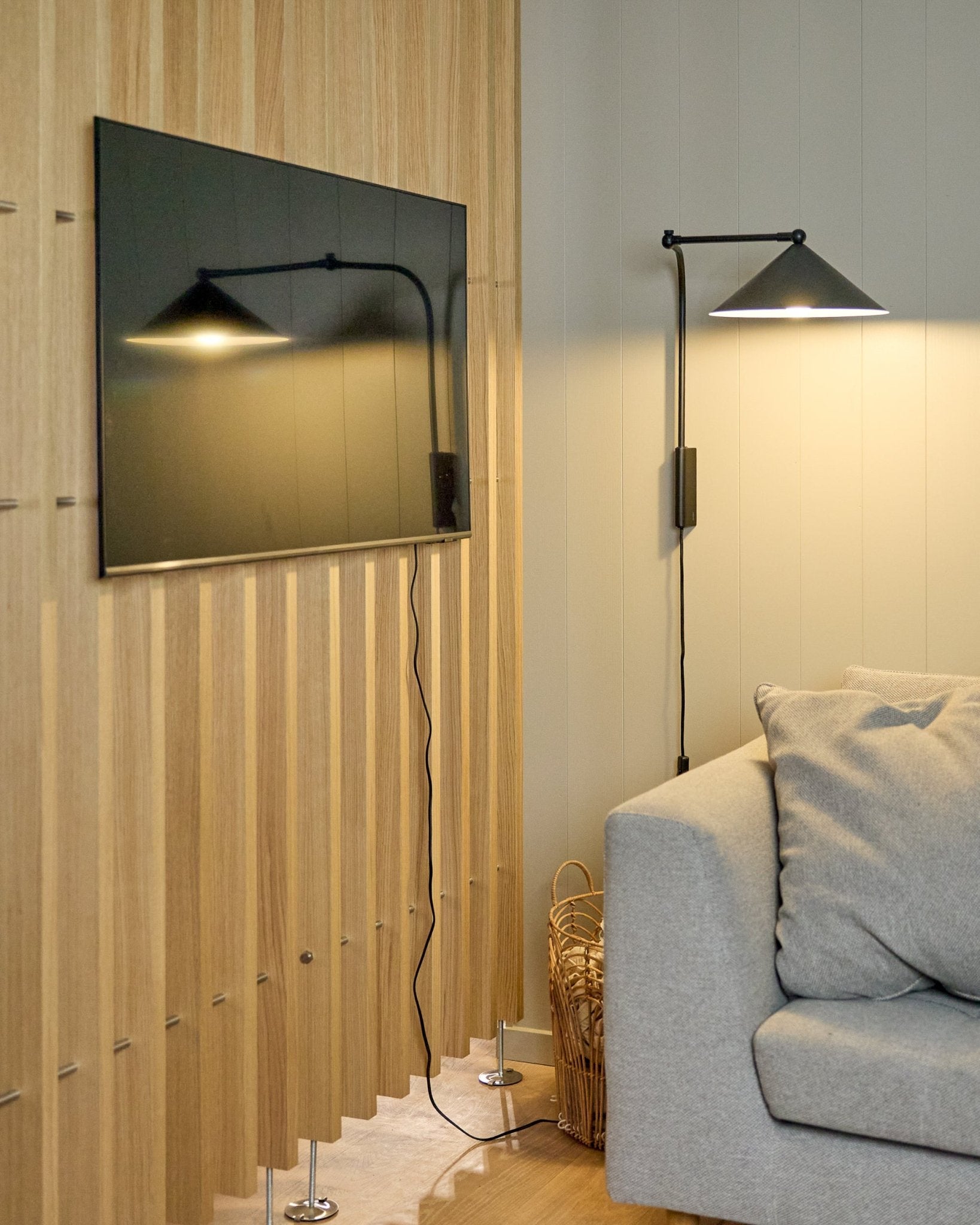 Le Nell | TV-Mount / BM1 de WoodUpp (Beige, 64x44 cm) fixe un téléviseur à écran plat sur un panneau Panneau acoustique nordique à côté d’un canapé gris ; un panier se trouve à proximité.