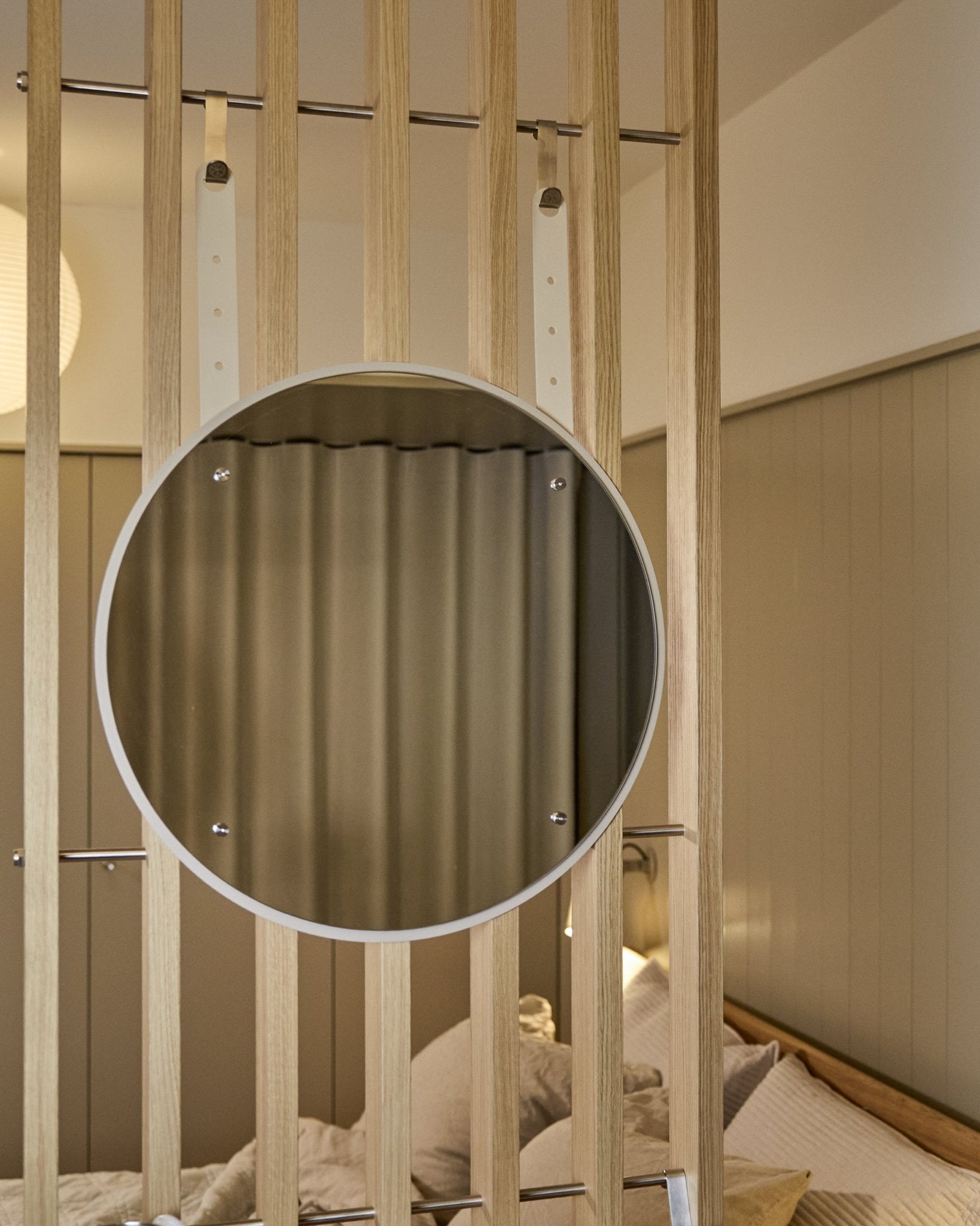 Le miroir rond Vala BM1 de WoodUpp, réglable en hauteur, 54 cm de diamètre, monté sur un panneau acoustique à lattes de bois vertical, avec un éclairage doux aux tons neutres.
