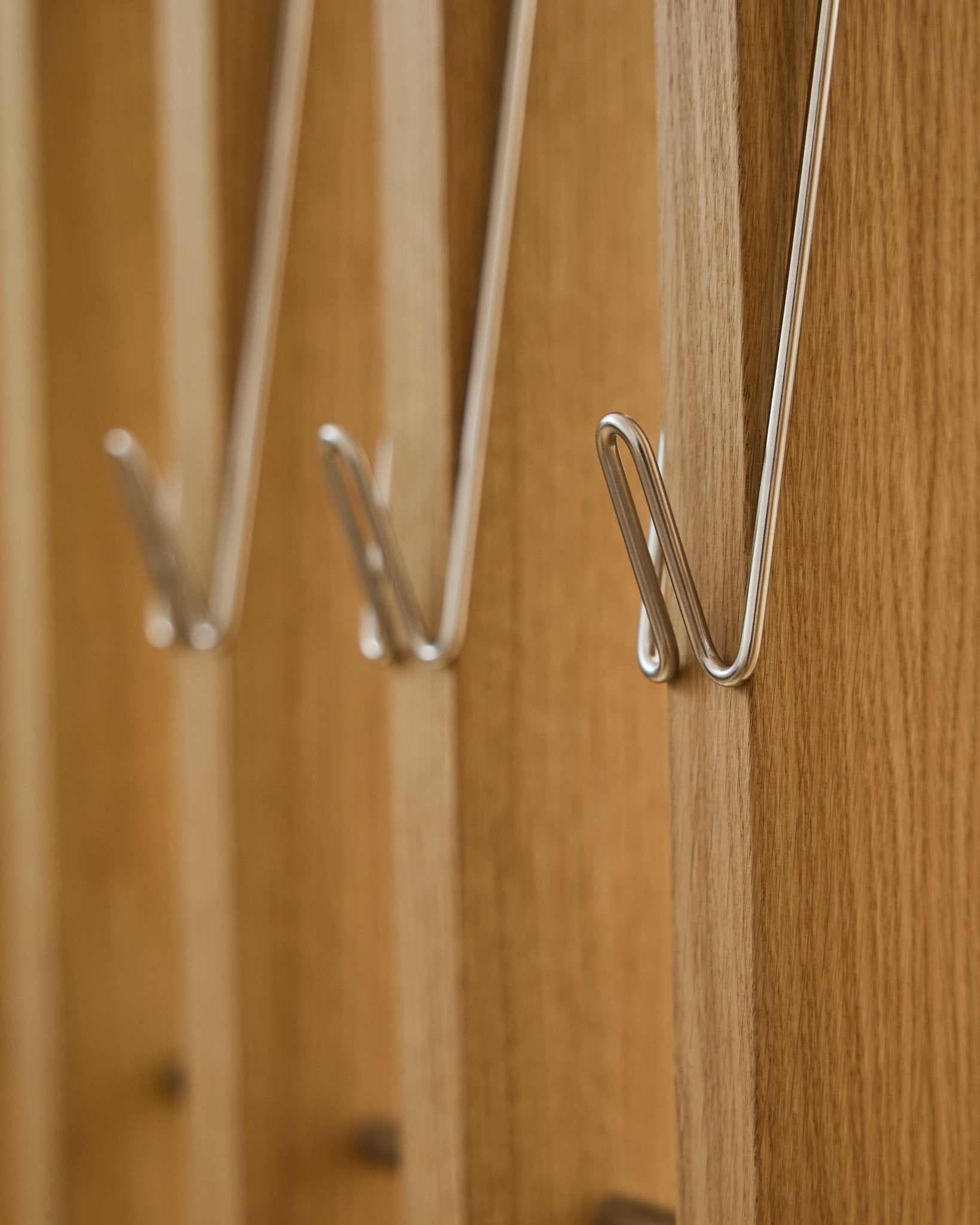 Gros plan sur trois Alva | Wire Hook / BM1, en Steel inoxydable, version longue, par WoodUpp, montés en ligne sur des panneaux acoustiques en bois Akupanel et projetant de douces ombres.