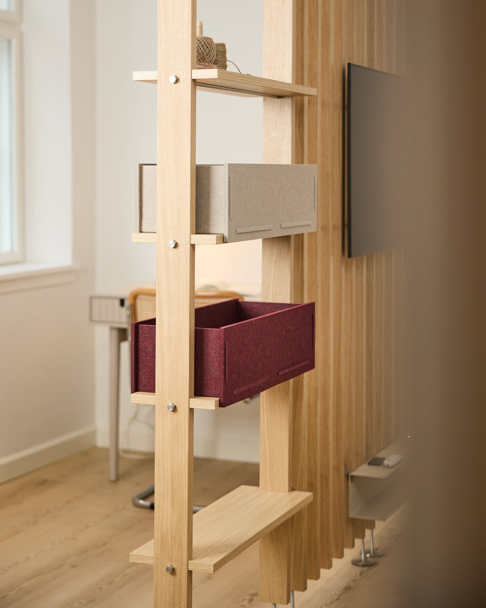 Une étagère WoodUpp présente une boîte de rangement beige et une ox red Vigg Felt Box / BM2 dans une pièce nordique lumineuse et minimaliste avec des détails acoustiques en bois.