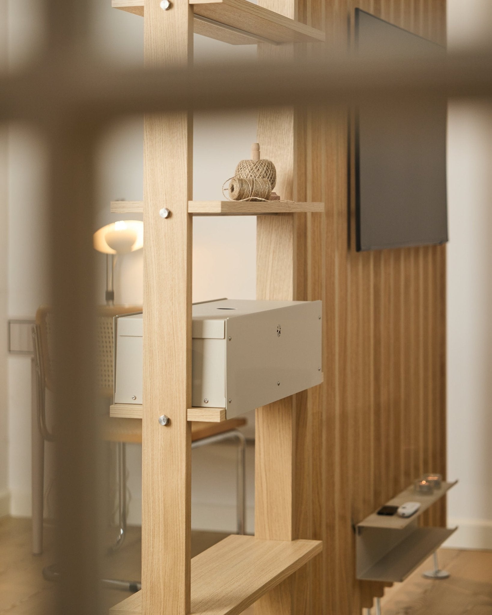 Une pièce cosy avec une chaise, une lampe et une TV met en scène l’étagère Nell | Metal Box / BM2 de WoodUpp, finition beige, dans un décor nordique minimaliste.