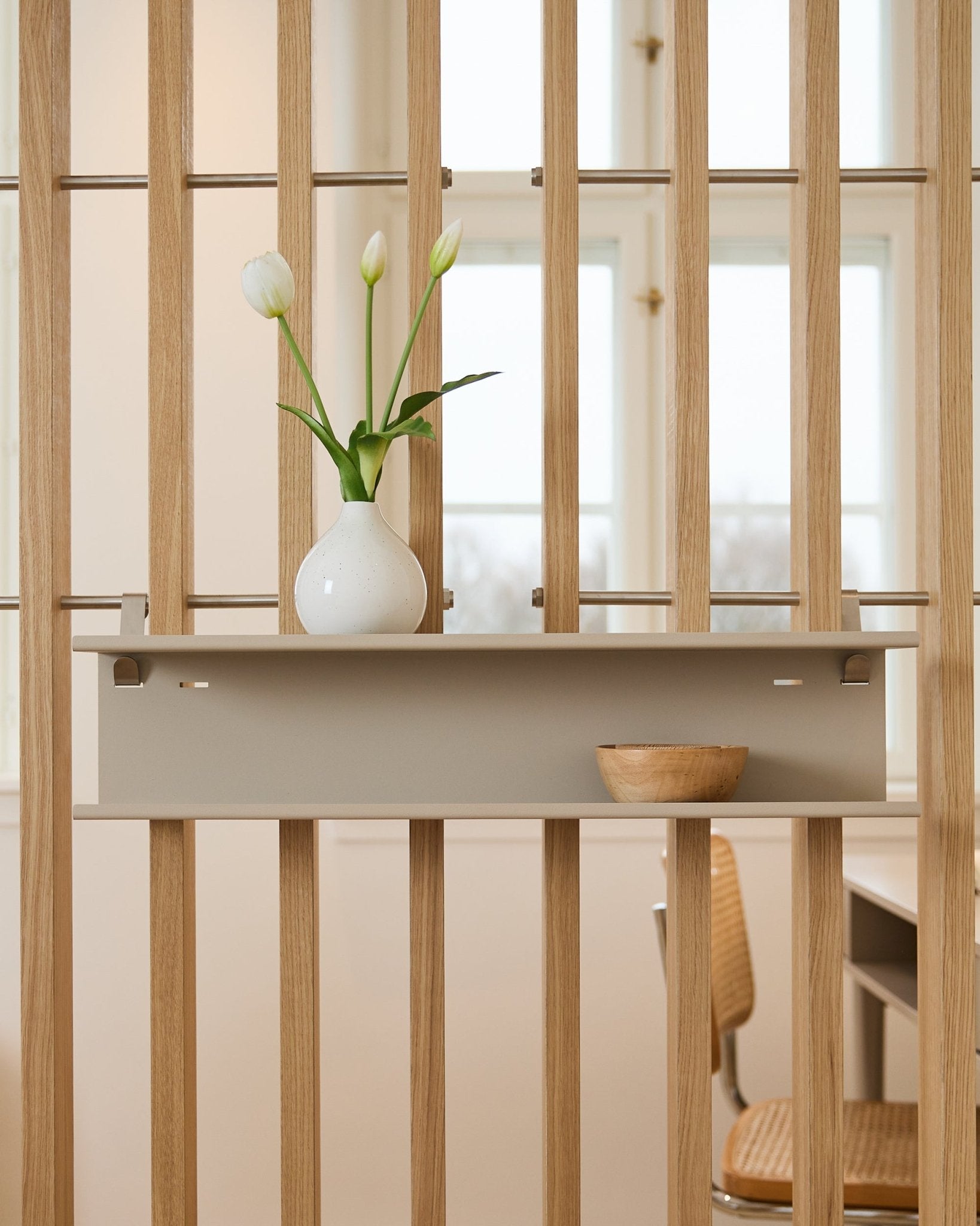 Double Metal Shelf / BM1 de WoodUpp en beige (63,5 cm) montée sur un séparateur de pièce à lattes, mise en scène avec un vase et un bol en bois.