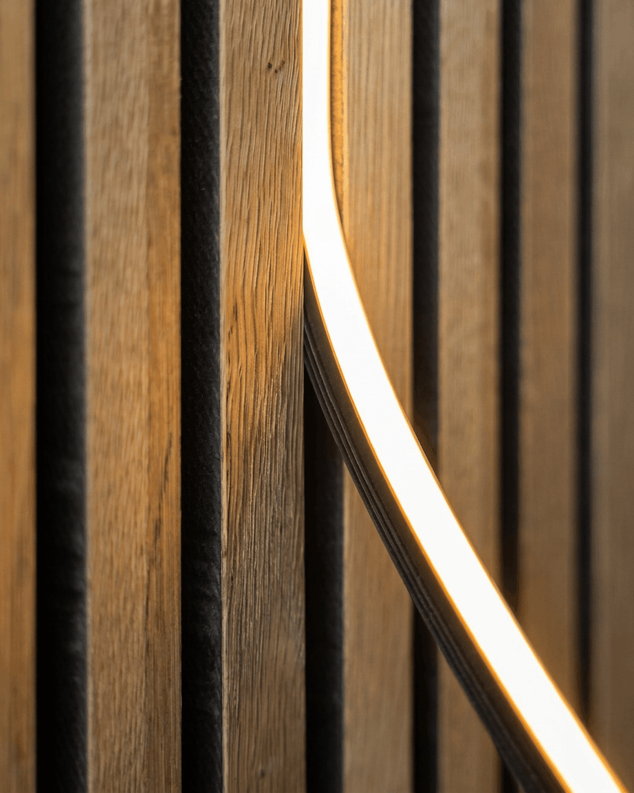Gros plan sur la bande LED Lumi (240 cm, Black) de WoodUpp installée sur un panneau acoustique en bois Akupanel nordique ; compatible Philips Hue.